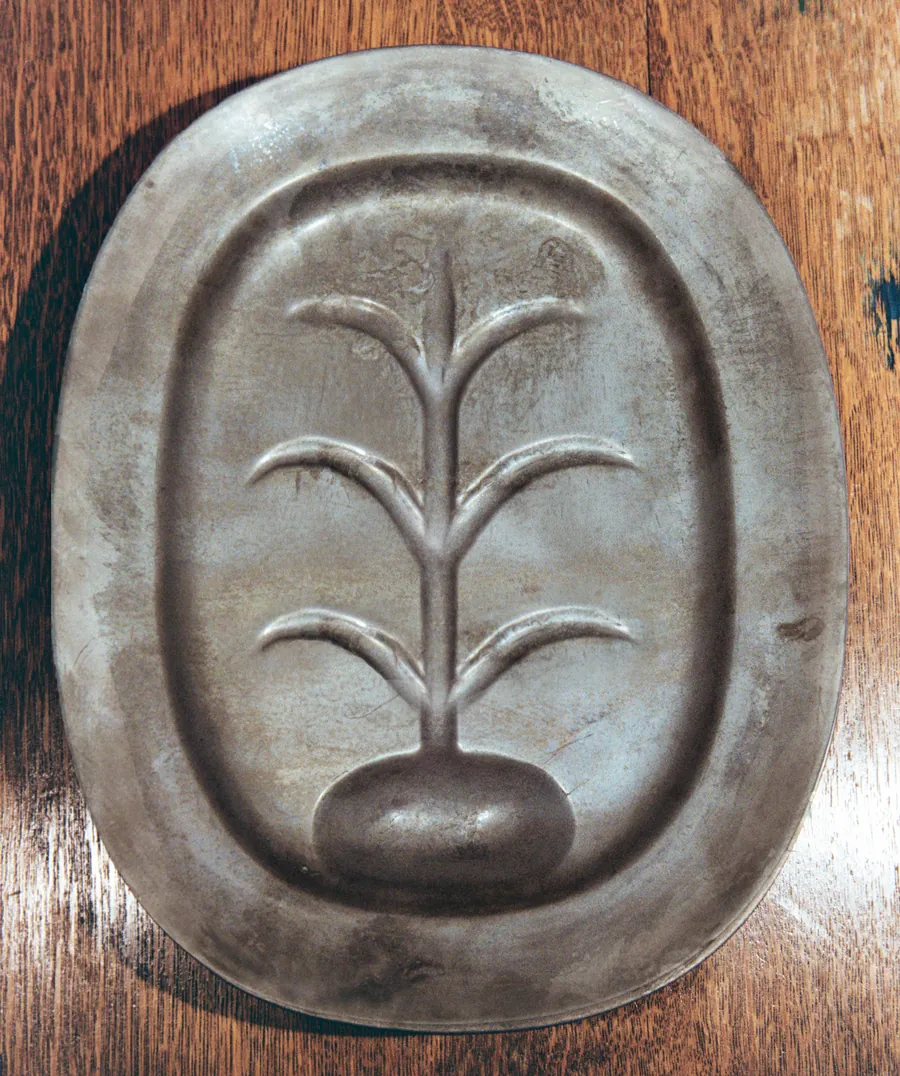 A pewter platter on a wooden table, three grilled sausages balanced on a carving fork