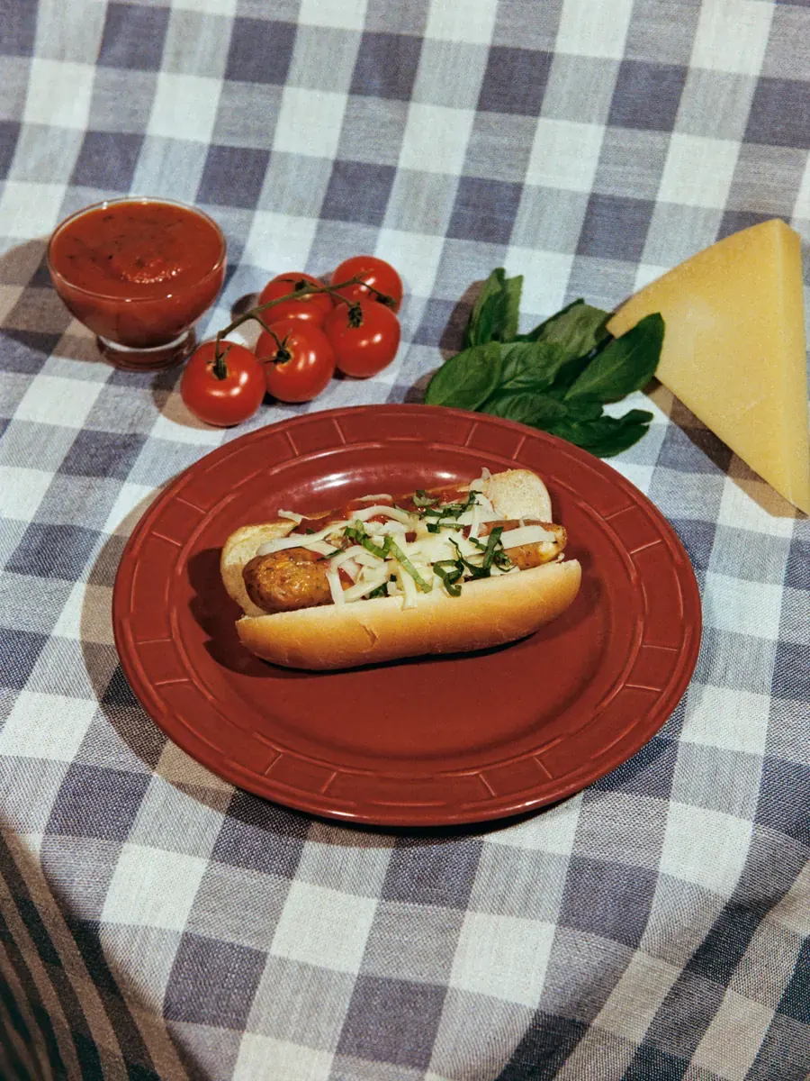 ParmaWürst on a bun with mozzarella and basil, beside marinara, tomatoes and Parmesan